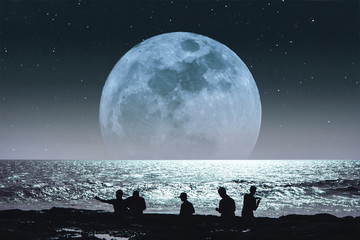 Silhouette group of people on the beach at night, with super full moon with stars on the sky. fairy tale fantasy landscape  