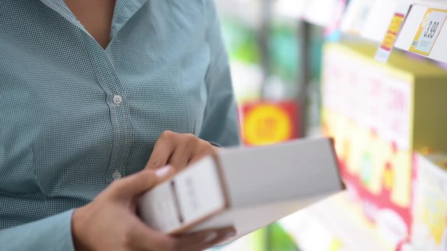 Woman doing grocery shopping at the supermarket, she is reading a product label and nutrition facts on a box