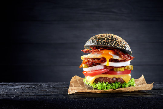 Black burger with egg and bacon on the wooden table