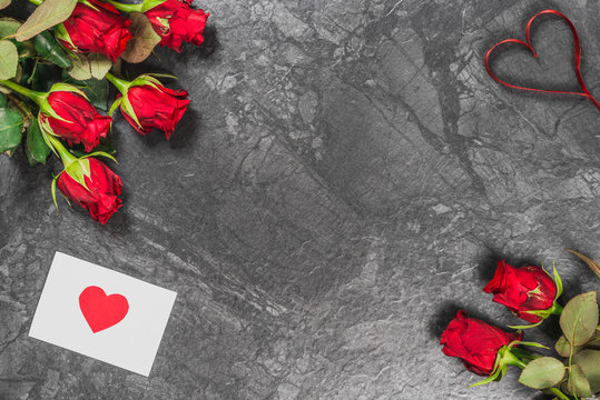 Red roses, ribbon and message card on black marble board. Valentines Day background