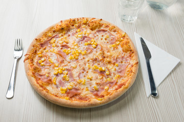 Pizza with ham and corn on the table
