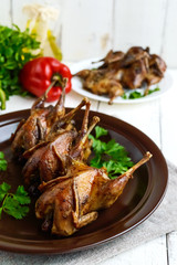 Roasted quail on a spit. Serving on a ceramic plate with greens. Close-up. Holiday menu.
