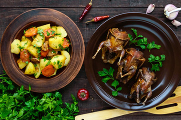 Roasted quail on a spit on a ceramic bowl with greens. Baked potato. The top view. Holiday menu.