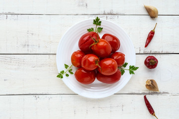 Juicy spicy marinated tomatoes on a white plate. On a light background, top view.