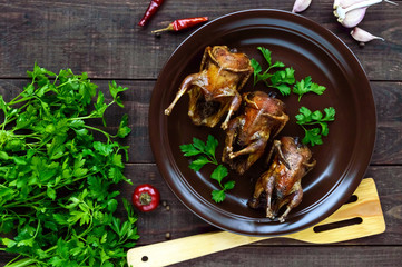 Roasted quail on a spit. Serving on a ceramic plate with greens. The top view. Holiday menu.