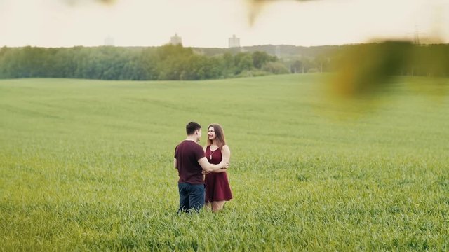 Loving couple hug, standing in a field. They smile happily, look at each other, hold hands. Slow mo