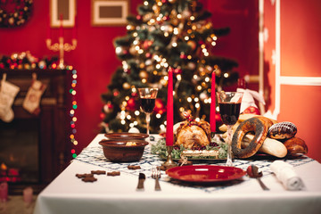 Christmas dinner by candlelight, table setting. Thanksgiving table with baked turkey in a decorated room with a Christmas tree.
