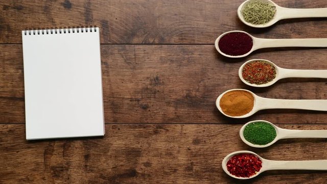 Spices in spoons moving forward to notebook over wooden background Stop motion animation