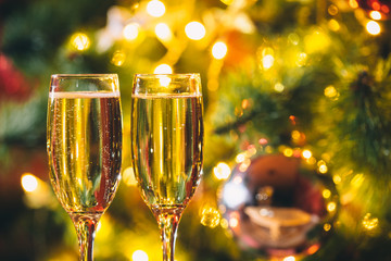 Beautiful two glasses of champagne standing on the table in the background of a blurred room with a decorated Christmas tree and fireplace. Soft focus. Shallow DOF