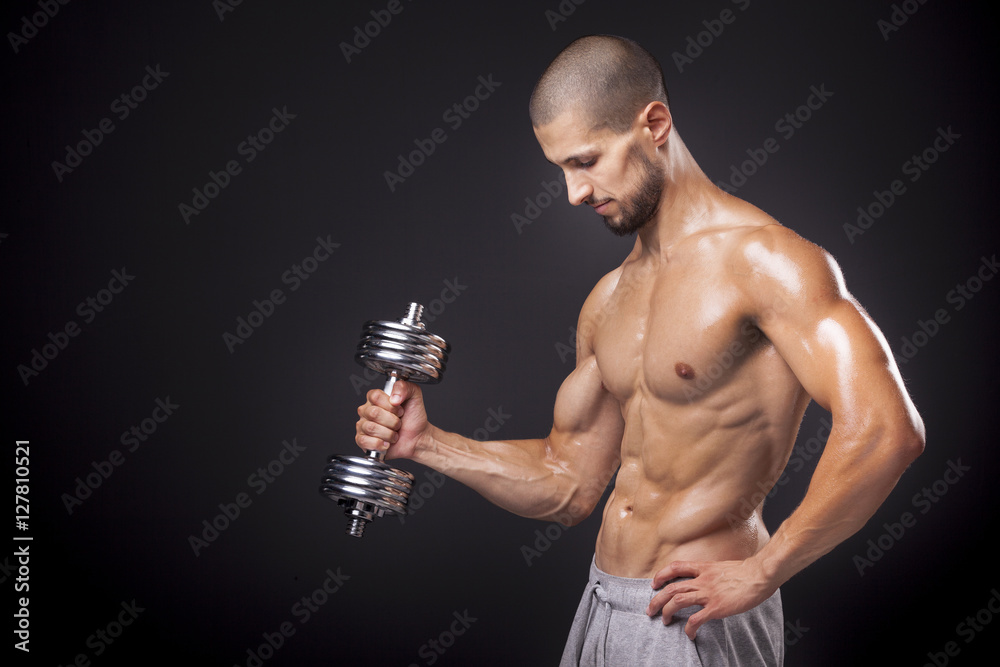 Wall mural young athletic man lifting weights over dark background