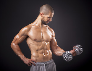 Fototapeta na wymiar Young muscular man lifting weights over dark background