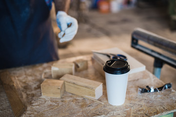 Modern carpentry work place with tablet, coffee, scissors and wooden pieces on table, in workshop