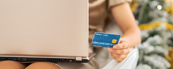 Closeup on credit card in hand of woman with laptop sitting in f