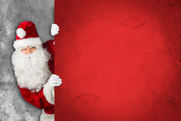 Santa claus hiding and looking behind empty red concrete billboard wall 