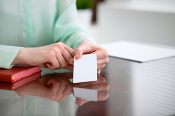 Business woman hands in a green blouse sitting at a desk in an office and holds out business card.