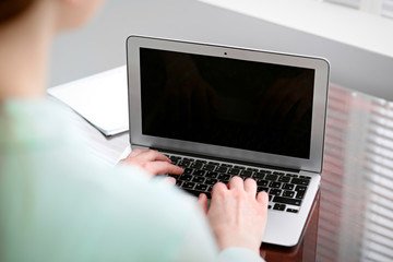 Business woman hands in a green blouse sitting at the desk in the office and typing on the laptop .