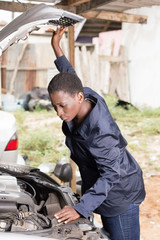 Mechanic looks into the engine of a car parked in her   workshop. 