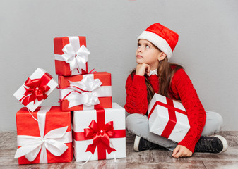 Pensive little girl in santa claus hat with present box