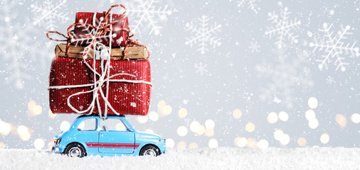 Blue retro toy car delivering Christmas or New Year gifts on festive gray background - 127815941