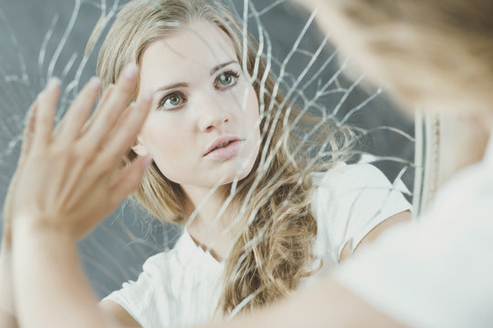Teenage girl touching broken mirror