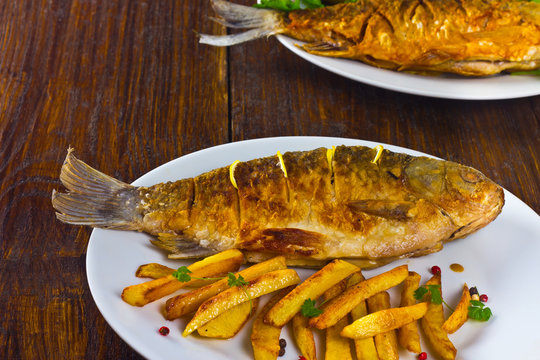 fried fish with fries on a white plate on a wooden table