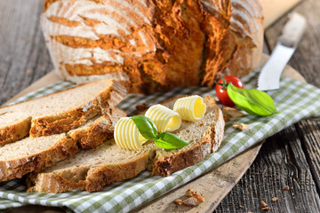 Frisches Steinofenbrot mit Butterröllchen auf einem altem Backbrett serviert - Fresh stone oven...