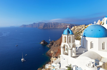 Fototapeta na wymiar Greece. Santorini Island. The small town Oia. The Orthodox Church with the traditional blue domes and white plastered walls on the steep bank of Aegean Sea