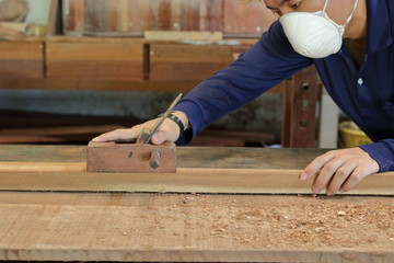 Carpenter working with a hand planer on  a plank of wood in carpentry workshop. He is wearing safety equipment .