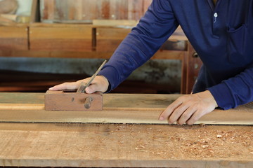 Hand of worker working with a hand planer on  a plank of wood.