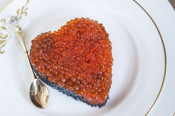 Christmas composition with Salmon roe and caviar in form of heart on white plate with beautiful little spoon 