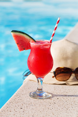 Fresh glass of water-melon smoothie drink with sunglasses, straw hat and slippers on border of a swimming pool - holiday tropical concept
