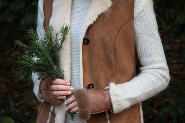 Girl in the warm, brown coat and leather gloves with fur holding spruce bouquet after harving .