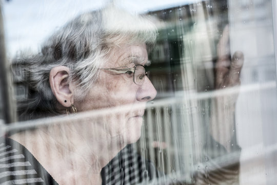 Senior woman looking out through a window like depress