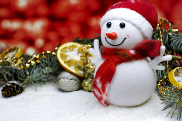 Christmas and New Year`s  red background with a toy snowman, dry oranges fruit, fir brunch, pin cone, walnut in snow