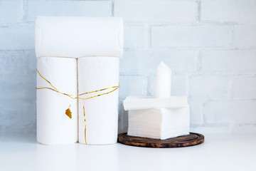 White paper towel rolls and paper napkins, tissue on white board against white brick wall background. Paper stack with decoration golden detail. Symbol of holiday celebration cooking. Copy space.
