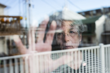 Senior woman looking out through a window like depress