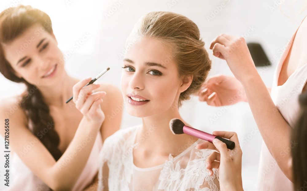 Wall mural Pleasant young bridesmaids helping the bride to get ready