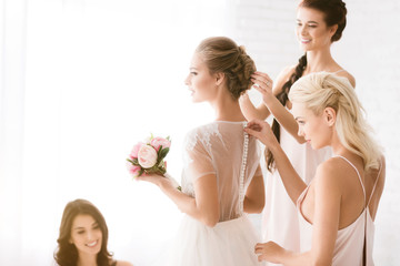 Delighted bridesmaids helping the bride to get ready