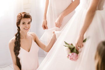 Obraz na płótnie Canvas Smiling young bridesmaid helping the bride to get ready