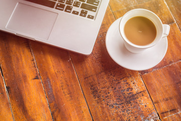 White coffee cup and laptop on wooden table top view