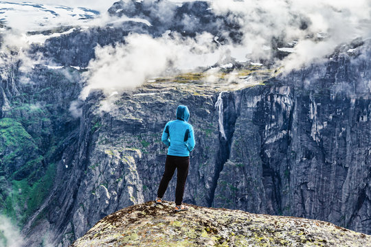 Young woman hiker wanderer staying at the edge of cliff in norwegian mountains above fjord and clouds. Norway, Scandinavia mountains. Wanderlust concept.