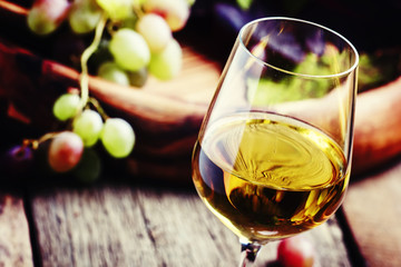 White wine in a glass with fall grapes, old wooden background, s