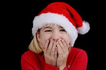 little girl with santa hat and hands over mouth excitement concept