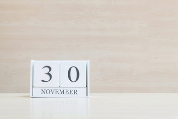 Closeup surface white wooden calendar with black 30 november word on blurred brown wood desk and wood wall textured background with copy space , selective focus at the calendar