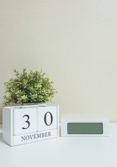 White wooden calendar with black 30 november word with clock and plant on white wood desk and cream wallpaper textured background , selective focus at the calendar