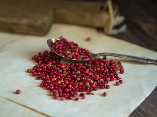 Pink pepper in a spoon and scattered on old sheets of paper on a wooden table
