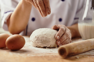 Woman baker powdering bread dough with flour. 