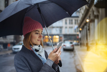 Happy smiling female talking with friends on video call outdoor, Young female reading text message on her mobile phone outdoor, Girl with an umbrella, Autumn landscape, Christmas lights