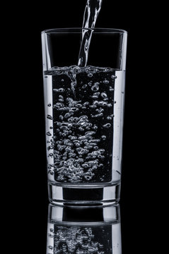 Pouring clear water in glass on black background