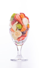 Colorful, healthy fruit salad in a large glass, on light background